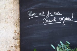 A blackboard in a cafe with the words "please ask to see our brunch menu!" written on it.