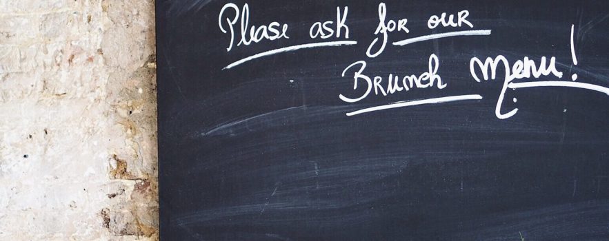 A blackboard in a cafe with the words "please ask to see our brunch menu!" written on it.